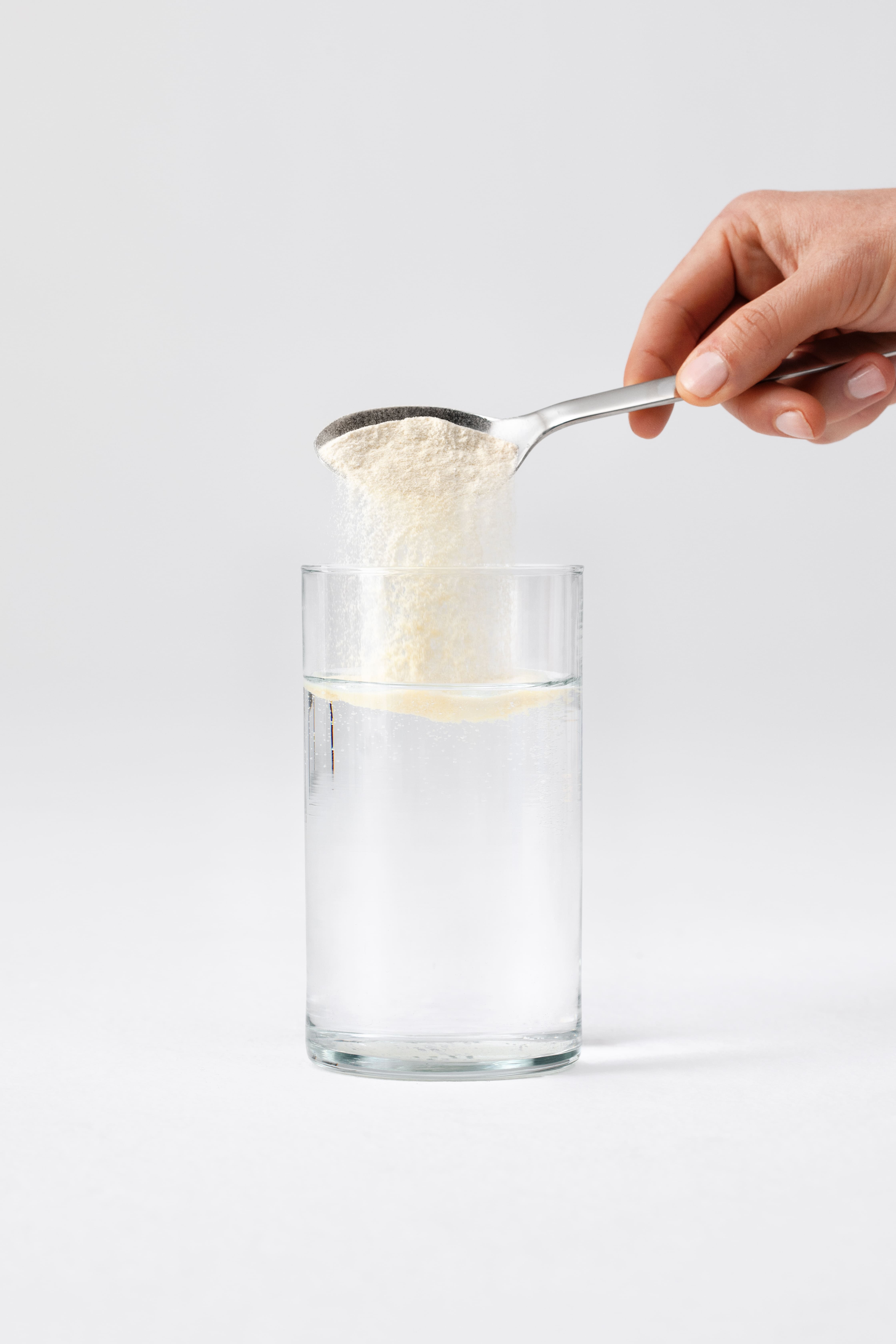 Hand schüttet Proteinpulver aus Messlöffel in Wasserglas